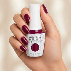 Mano sosteniendo el frasco de esmalte en gel Gelish Rendezvous, color Borgoñas acabado Cream, con las uñas pintadas del mismo tono