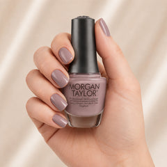 Mano sosteniendo el frasco de esmalte tradicional Morgan Taylor I Or-Chid You Not, color Mauves acabado Cream, con las uñas pintadas del mismo tono