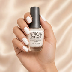 Mano sosteniendo el frasco de esmalte tradicional Morgan Taylor Sheek White, color Blancos acabado Cream, con las uñas pintadas del mismo tono