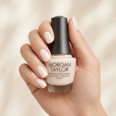Mano sosteniendo el frasco de esmalte tradicional Morgan Taylor Sweet On You, color Nudes acabado Cream, con las uñas pintadas del mismo tono