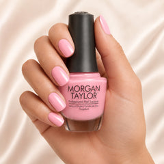 Mano sosteniendo el frasco de esmalte tradicional Morgan Taylor You're So Sweet You're Giving Me a Toothache, color Rosas acabado Cream, con las uñas pintadas del mismo tono